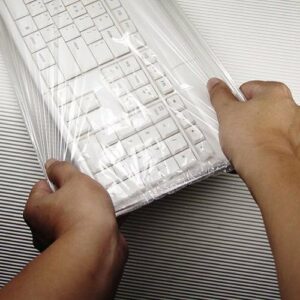two hands hold a white keyboard covered in a plastic film